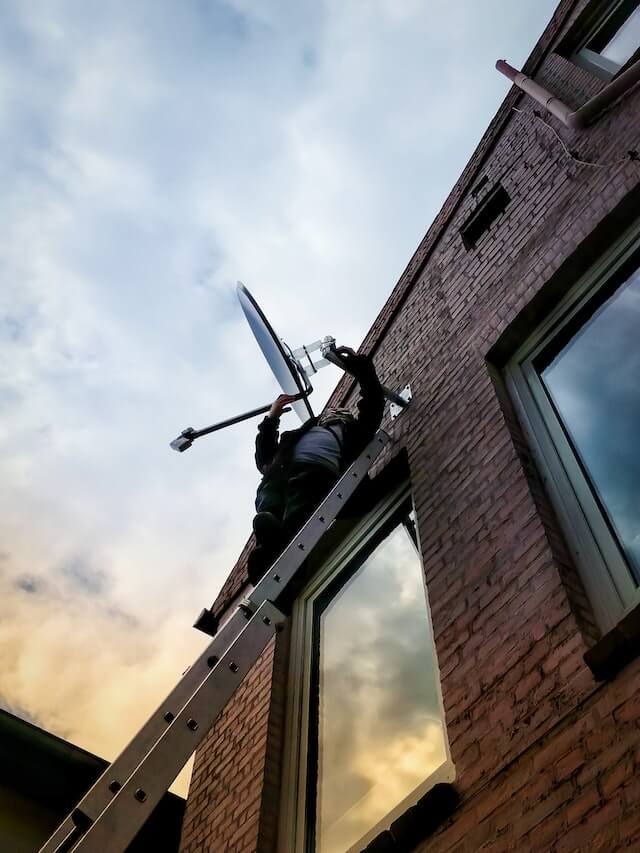 Man on a ladder installing satellite TV dish